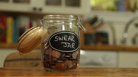 An anonymous person drops some loose change into a saving jar, which has Swear Jar written on it