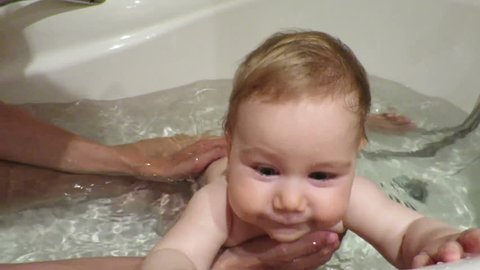 nine month old naked baby having a bath with mom in bathtub indoor 
