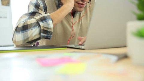 Young office worker using headphones in front of laptop