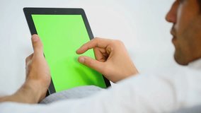 Man websurfing on digital tablet, green screen