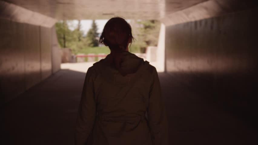 Woman walks through dark tunnel with light at the end of the tunnel