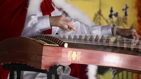 A woman in traditional costume playing guzheng.Guzheng is an traditional Chinese musical instrument,It belongs to the zither family of string instruments.
