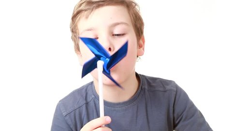 Little boy in gray T-shirt blows strongly on a plastic propeller, windmill and it turns quickly  