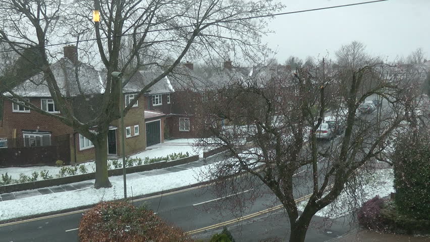 A man walks along a suburban street whilst snow is falling.