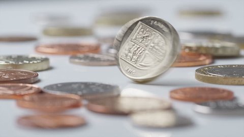 UK Currency one pound coin spinning amongst other UK currency coins in slow motion at 120fps, shot on RED EPIC