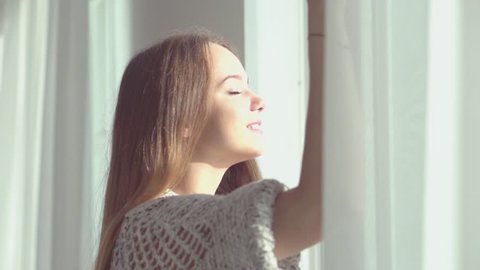 Young beautiful woman opening window and let the fresh air in the room. Cute girl looking out the window admiring outside view. Slow motion video footage high speed camera 240 fps. Slowmo 1920x1080