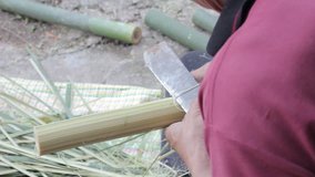 close-up of man using knife to split and shave small strips of bamboo 