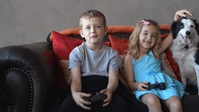 Children playing video game at home with pet dog on sofa couch