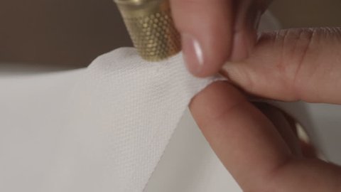 Super slow motion of middle-age woman hand sewing white fabric with needle,spread and thimble 