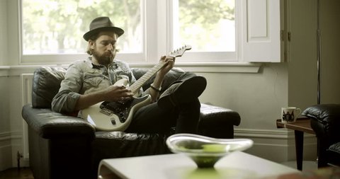 Man sitting on armchair and playing guitar Stockvideó
