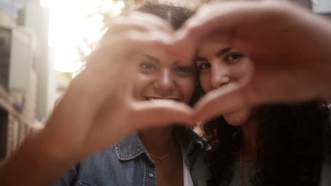 Best mixed race girl friends show heart shape to camera with hands: film stockowy