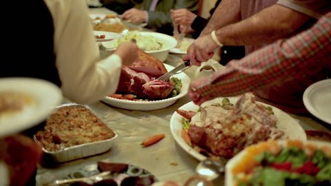 Thanksgiving Table with Turkey and Side Dishes and Man Carving, Slicing, and Serving Ham