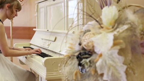 Beautiful focused girl in white dress plays white piano in light room