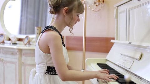 Happy girl in white dress plays white piano in light room