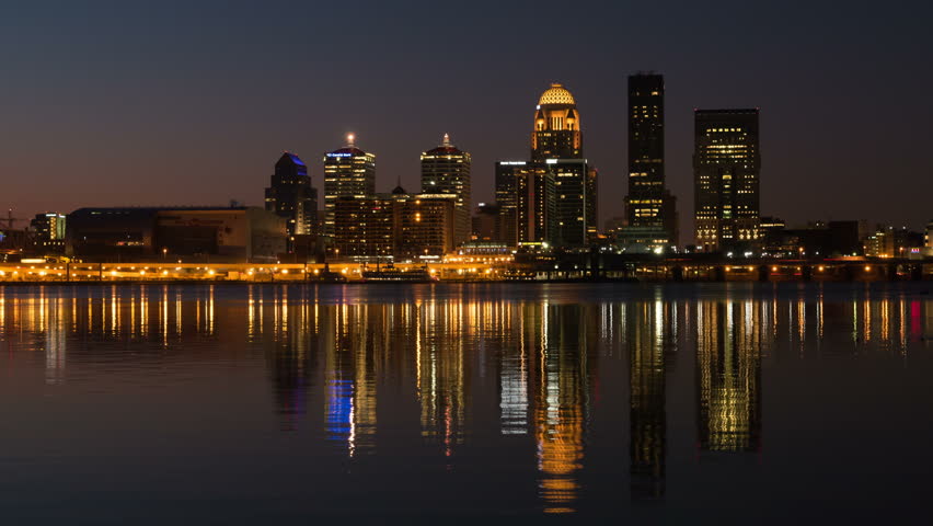 (Time-lapse/Zoom-in) The illuminated skyline of Louisville, Kentucky is reflected in the waters of the Ohio River as the sky lightens during morning twilight.