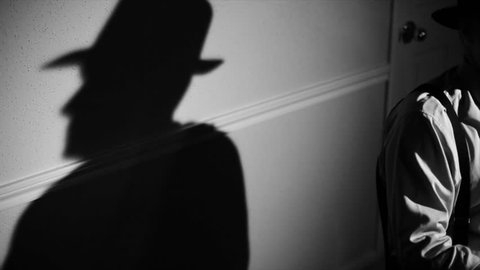 The camera pans from a stark shadow of a person to a man wearing a fedora and typing on a vintage 40's typewriter. Film Noir,