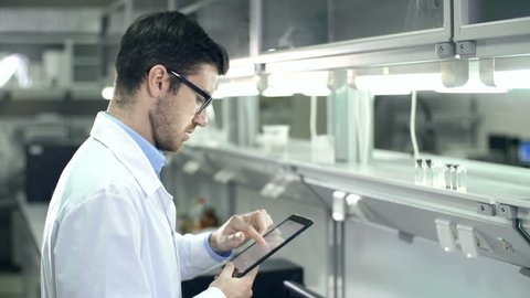 Laboratory worker checking the contents of glassware and inputting data to digital tablet