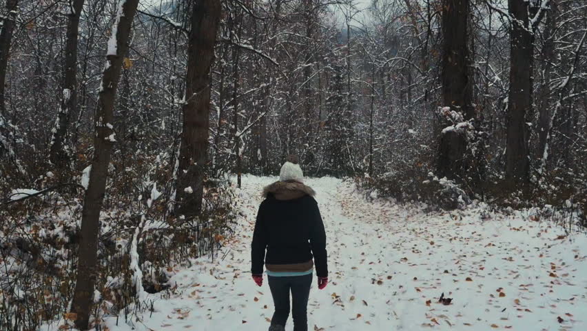 a girl walking on a snow path with a pan up towards the trees