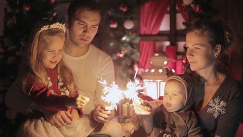 Beautiful happy family with two wonderful kids meet New Year with burning sparklers, laugh and kisses