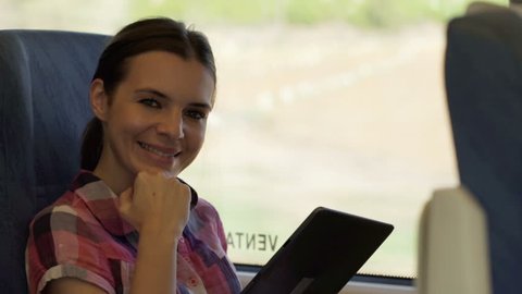 Portrait of beautiful, smiling woman with tablet during train ride 
