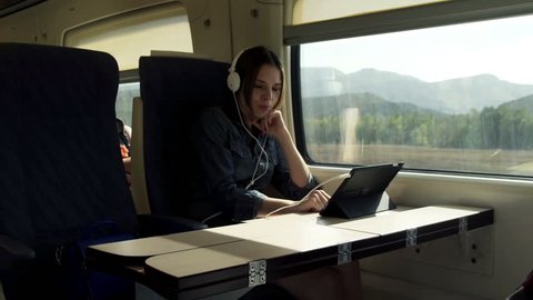 Young woman in headphones watching funny movie on tablet during train ride 
