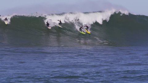 Four male surfers catch a big wave, one falls. at Mavericks, CA. Jet skis and boat in foreground.
