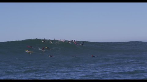Two male surfers catch big wave at Mavericks, CA. Jet skis with filmers and boat in foreground.