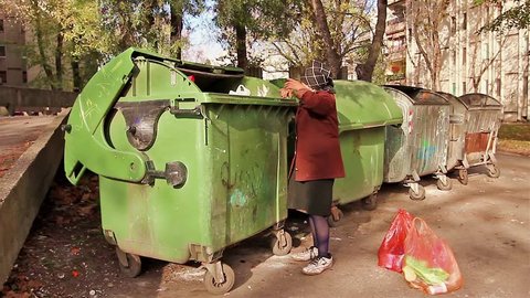 Homeless woman is searching for food in garbage dumpster/Woman in poverty/Woman in poverty is searching something in container.
