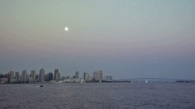 Time lapse video of moon rising over San Diego Bay at twilight with downtown cityscape and passing boats