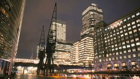 Night time lapse of London Canary Wharf financial district taken on a cold winter night. DLR in the background. Canal visible and silhouettes of people walking pass. Logos digitally removed.