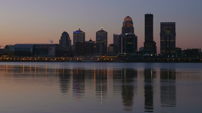 The illuminated skyline of Louisville, Kentucky is reflected in the waters of the Ohio River as the sky lightens during morning twilight.
