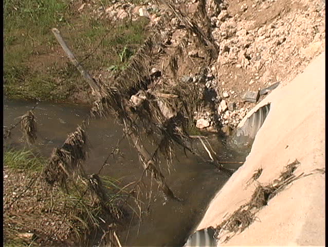 A swiftly flowing stream with snags in a fence bouncing back and forth
