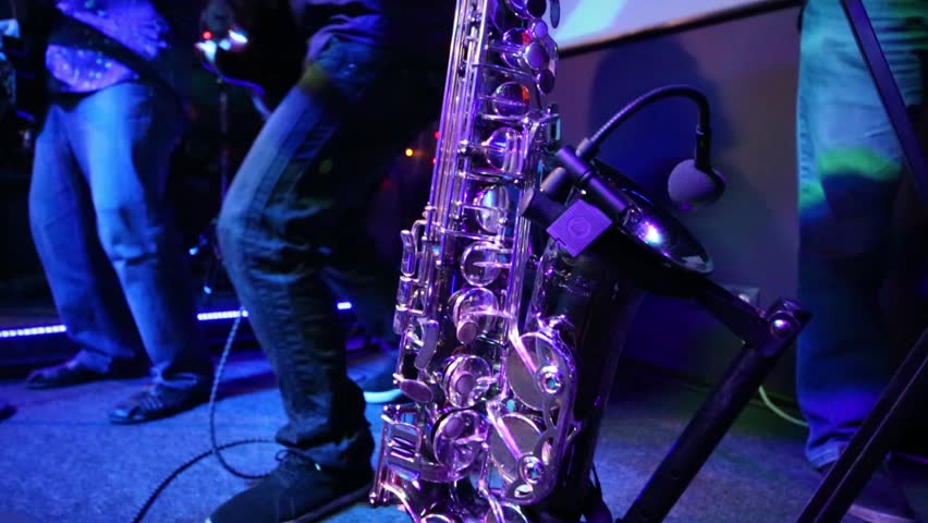 Group of three middle aged musicians perform at stage with shining saxophone