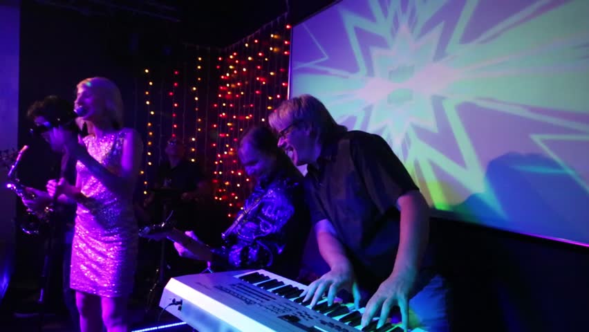 Band of four men with sax and singing blonde pretty woman performs on stage