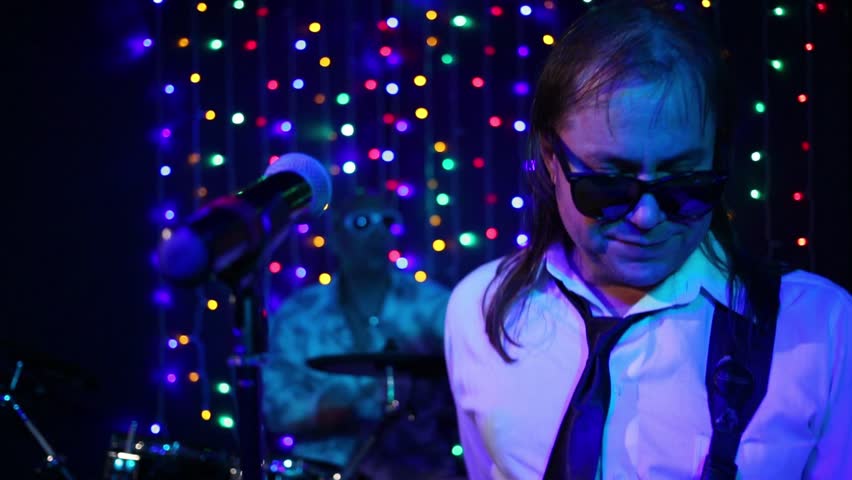 Guitarist in sunglasses near microphone and drummer out of focus