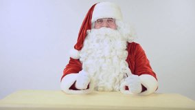 Santa Claus sitting at the table and gestures. on a white background