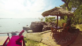 FullHD video - Panoramic view of the tropical sea from a terrace at a resort in Sihanoukville. Picnic tables and a grass umbrella are visible in the foreground.