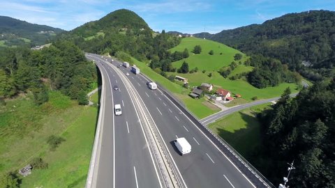 Highway road traffic on a bridge in a valley . Aerial shoot of a highway road with traffic cars and trucks in a valley with green grass field and trees in nature full of small hills