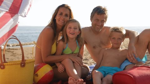 Family in swimwear on the beach Mom and Dad sitting under an umb