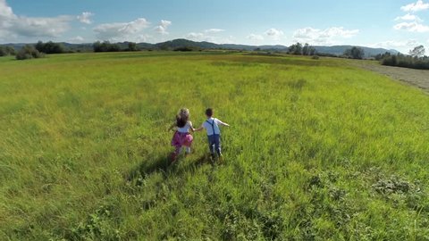 Lovely kids couple running on a grass field. Aerial slow motion shoot of a couple kids holding hands running happily on a grass field free lik a bird