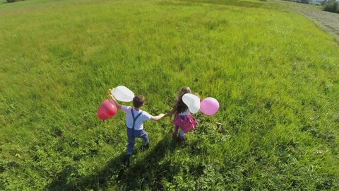 running couple kids with balloons . Aerial slow motion shoot of couple kids, boy and girl holding their hands lovely free running with balloons in their hands