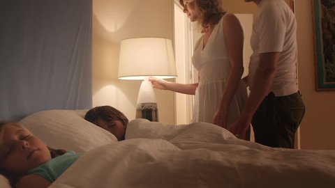 Couple Tucking Their Children Into Bed.