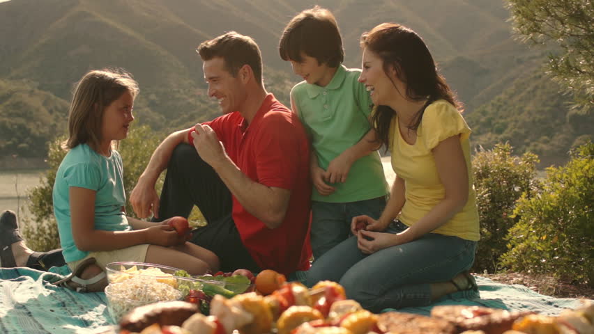 Dolly Shot Of Family Having Barbecue Picnic By Lake In Countryside.
