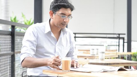 Indian businessman having lunch at outdoor cafeteria, drinking milk tea and reading newspaper