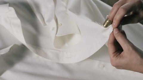 Super slow motion of middle-age woman hand sewing white shirt buttonhole with needle,spread and thimble (macro closeup)