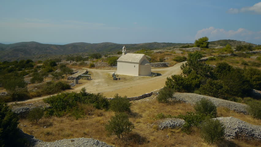 Aerial view from behind of small white church on island hill with beautiful prospect landscape and distant sea lagoons.