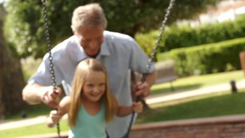 Slow-Motion Of Grandfather Pushing Granddaughter On Swing In Park.