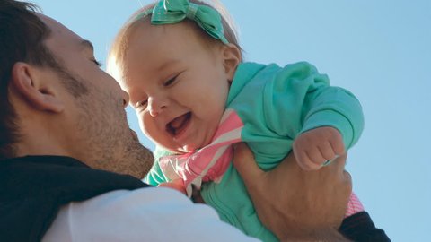 Dad throws up his sweet daughter baby with a bow on her head, baby rejoices and laughs: film stockowy