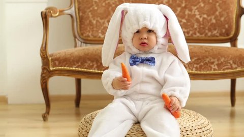 Baby boy in white costume of rabbit sits and holds carrot