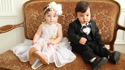 Beautiful babies in costumes of bride and groom sit on vintage couch 庫存影片